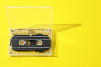 Photo of One audio cassette in open box on yellow background, above view. Space for text