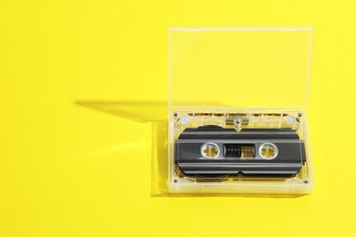 Photo of One audio cassette in open box on yellow background, above view. Space for text