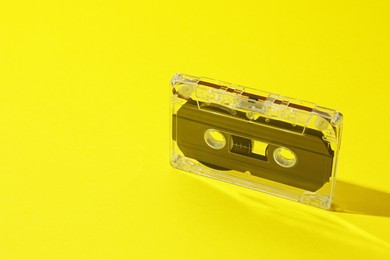 Photo of One audio cassette with magnetic tape on yellow background, closeup. Space for text