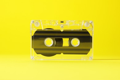 Photo of One audio cassette with magnetic tape on yellow background, closeup
