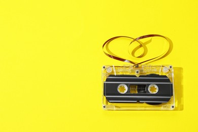 Photo of One audio cassette with heart shaped magnetic tape on yellow background, top view. Space for text