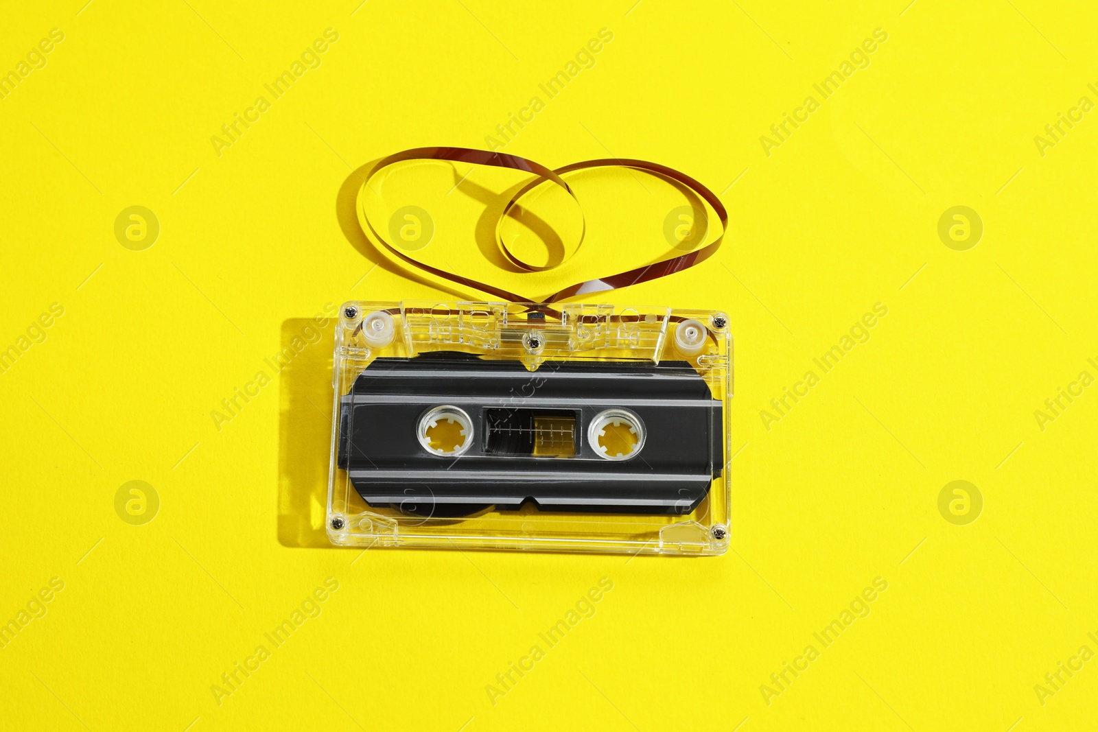 One audio cassette with heart shaped magnetic tape on yellow background, above view Photo of One audio cassette with heart shaped magnetic tape on yellow background, above view
