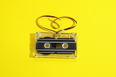 Photo of One audio cassette with heart shaped magnetic tape on yellow background, above view