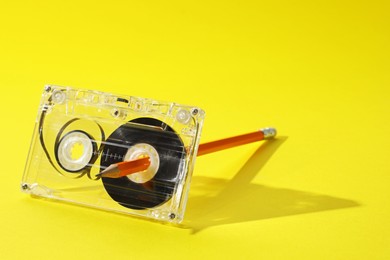 Photo of Rewinding audio cassette with pencil on yellow background, closeup. Space for text