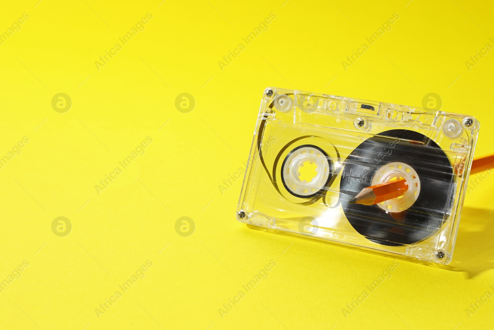Rewinding audio cassette with pencil on yellow background, closeup. Space for text Photo of Rewinding audio cassette with pencil on yellow background, closeup. Space for text