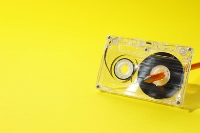 Photo of Rewinding audio cassette with pencil on yellow background, closeup. Space for text
