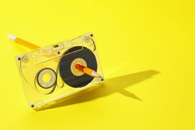 Photo of Rewinding audio cassette with pencil on yellow background, closeup. Space for text