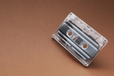 Photo of One audio cassette with magnetic tape on brown background, closeup. Space for text