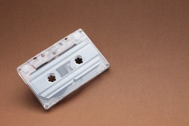 Photo of One audio cassette with magnetic tape on brown background, above view. Space for text