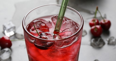 Photo of Tasty cherry soda with ice cubes and berry in glass on grey table, closeup