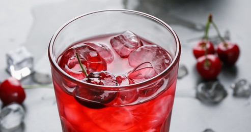 Photo of Tasty cherry soda with ice cubes and berry in glass on grey table, closeup