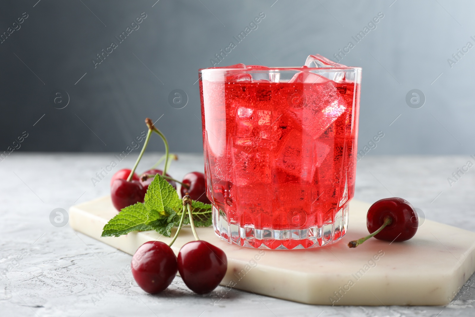 Tasty cherry soda with ice cubes, berries and mint in glass on grey textured table, closeup Photo of Tasty cherry soda with ice cubes, berries and mint in glass on grey textured table, closeup