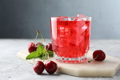 Photo of Tasty cherry soda with ice cubes, berries and mint in glass on grey textured table, closeup