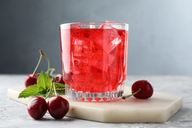 Photo of Tasty cherry soda with ice cubes, berries and mint in glass on grey textured table, closeup