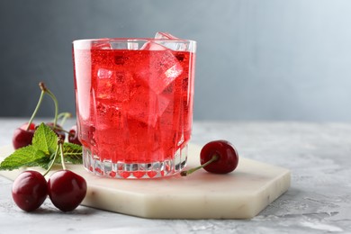 Photo of Tasty cherry soda with ice cubes, berries and mint in glass on grey textured table, closeup. Space for text