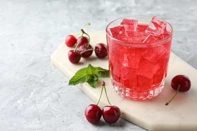 Photo of Tasty cherry soda with ice cubes, berries and mint in glass on grey textured table, closeup. Space for text