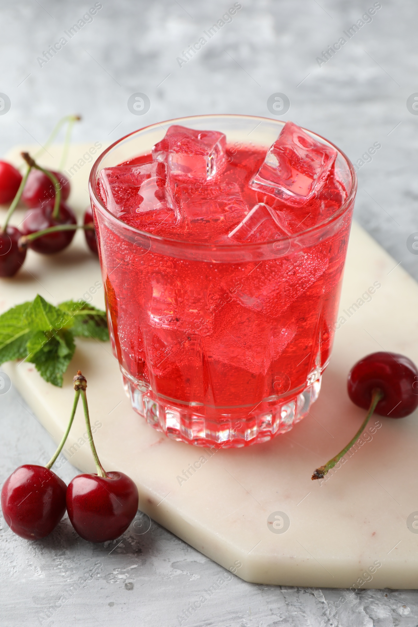 Tasty cherry soda with ice cubes, berries and mint in glass on grey textured table, closeup Photo of Tasty cherry soda with ice cubes, berries and mint in glass on grey textured table, closeup