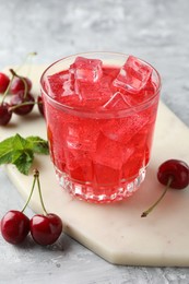 Photo of Tasty cherry soda with ice cubes, berries and mint in glass on grey textured table, closeup