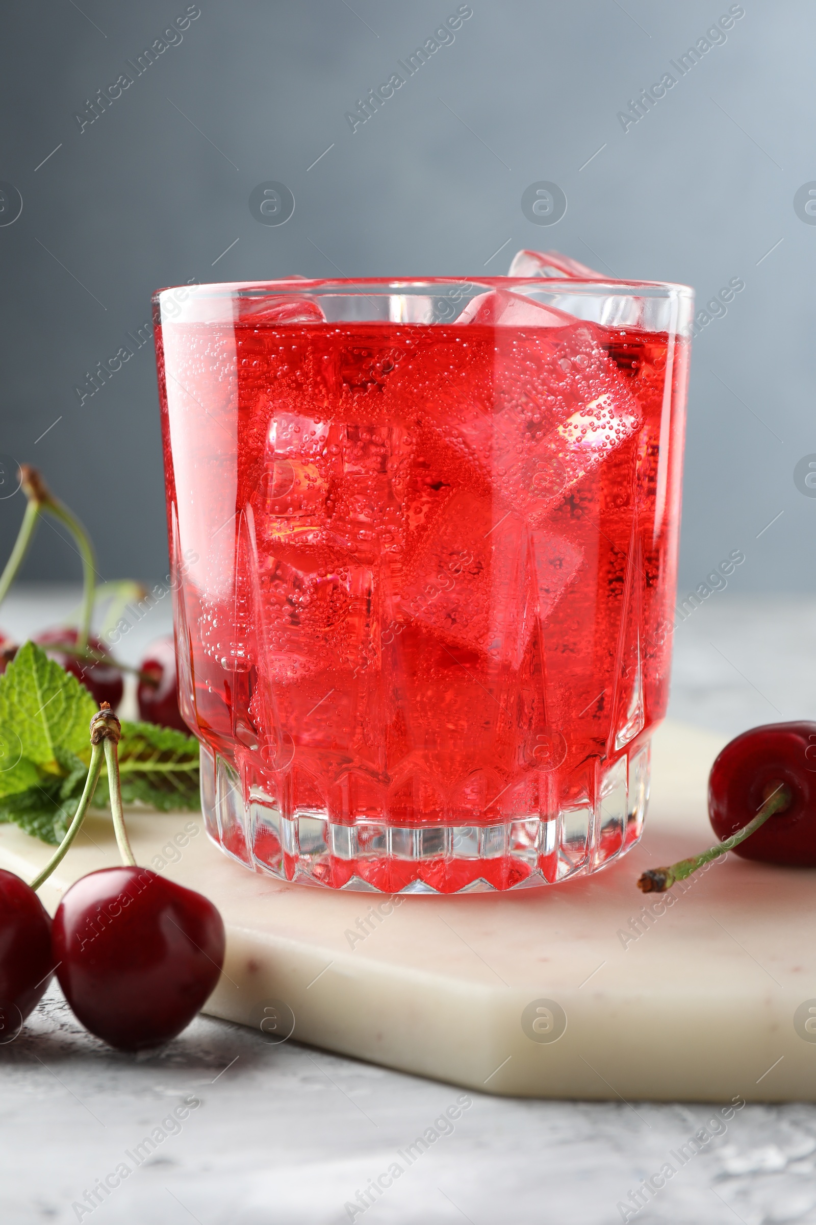 Tasty cherry soda with ice cubes, berries and mint in glass on grey textured table, closeup Photo of Tasty cherry soda with ice cubes, berries and mint in glass on grey textured table, closeup