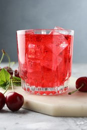 Photo of Tasty cherry soda with ice cubes, berries and mint in glass on grey textured table, closeup