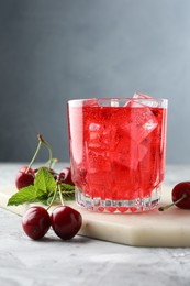Photo of Tasty cherry soda with ice cubes, berries and mint in glass on grey textured table, closeup