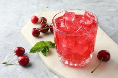 Photo of Tasty cherry soda with ice cubes, berries and mint in glass on grey textured table, closeup
