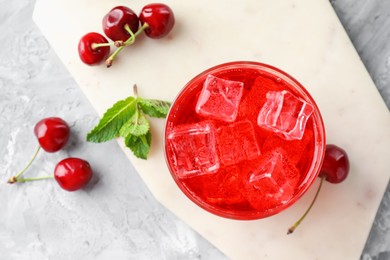 Photo of Tasty cherry soda with ice cubes, berries and mint in glass on grey textured table, flat lay