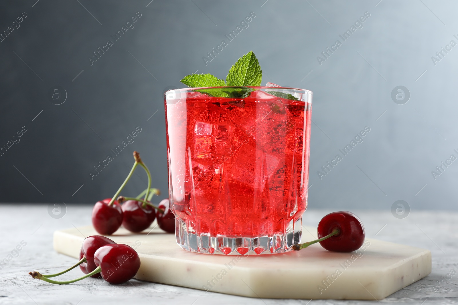 Tasty cherry soda with ice cubes, berries and mint in glass on grey textured table, closeup Photo of Tasty cherry soda with ice cubes, berries and mint in glass on grey textured table, closeup