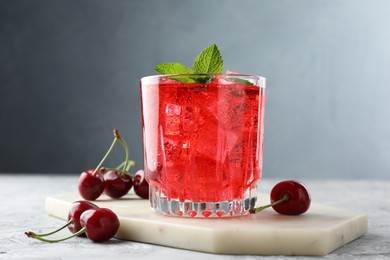Photo of Tasty cherry soda with ice cubes, berries and mint in glass on grey textured table, closeup