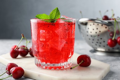 Photo of Tasty cherry soda with ice cubes, berries and mint in glass on grey textured table, closeup