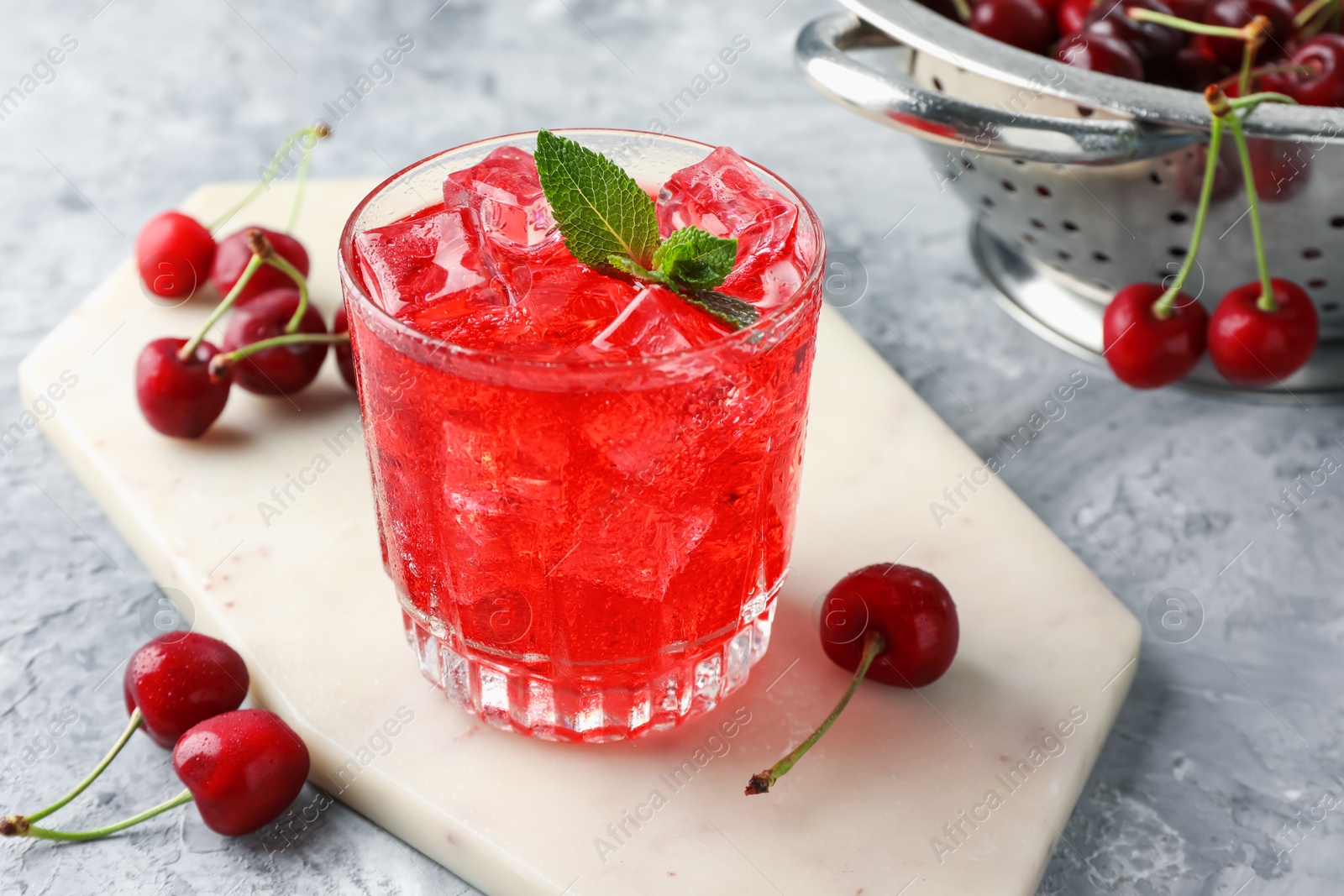Tasty cherry soda with ice cubes, berries and mint in glass on grey textured table, closeup Photo of Tasty cherry soda with ice cubes, berries and mint in glass on grey textured table, closeup