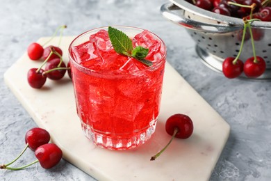Photo of Tasty cherry soda with ice cubes, berries and mint in glass on grey textured table, closeup