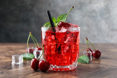 Photo of Tasty cherry soda with ice cubes, berries and mint in glass on wooden table, closeup
