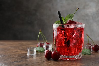Photo of Tasty cherry soda with ice cubes, berries and mint in glass on wooden table, closeup. Space for text