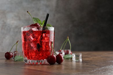 Photo of Tasty cherry soda with ice cubes, berries and mint in glass on wooden table, closeup. Space for text