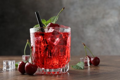 Photo of Tasty cherry soda with ice cubes, berries and mint in glass on wooden table, closeup. Space for text