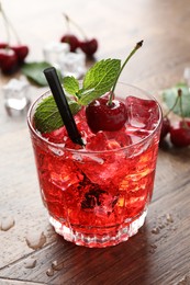 Photo of Tasty cherry soda with ice cubes, berries and mint in glass on wooden table, closeup