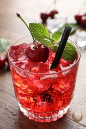 Photo of Tasty cherry soda with ice cubes, berries and mint in glass on wooden table, closeup