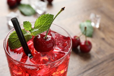 Photo of Tasty cherry soda with ice cubes, berries and mint in glass on wooden table, closeup. Space for text