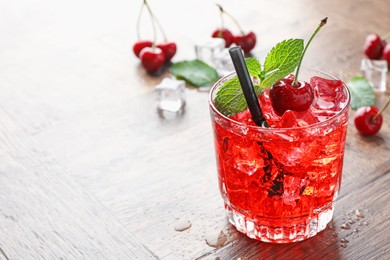 Photo of Tasty cherry soda with ice cubes, berries and mint in glass on wooden table, closeup. Space for text