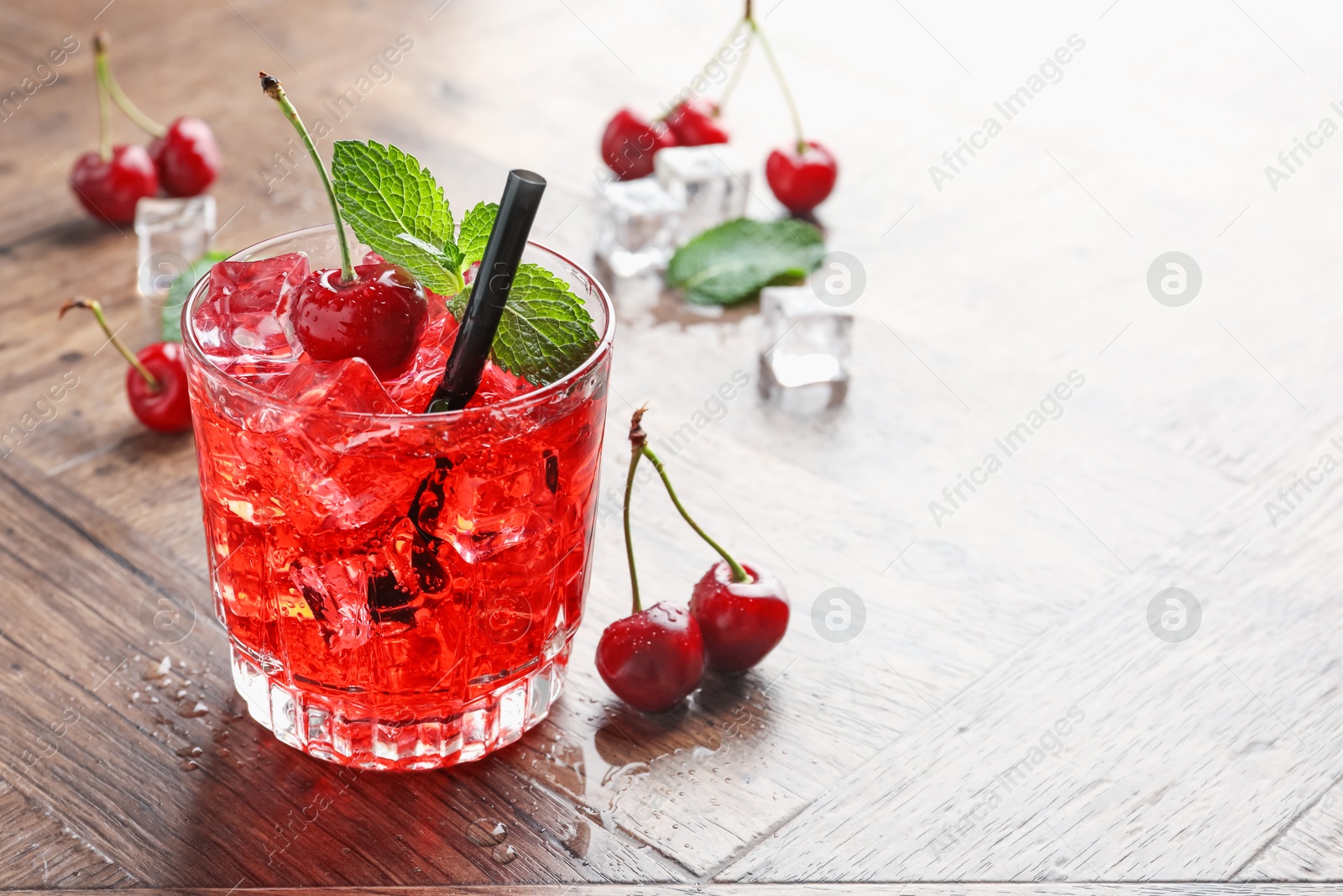 Tasty cherry soda with ice cubes, berries and mint in glass on wooden table, closeup. Space for text Photo of Tasty cherry soda with ice cubes, berries and mint in glass on wooden table, closeup. Space for text