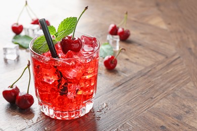 Photo of Tasty cherry soda with ice cubes, berries and mint in glass on wooden table, closeup. Space for text