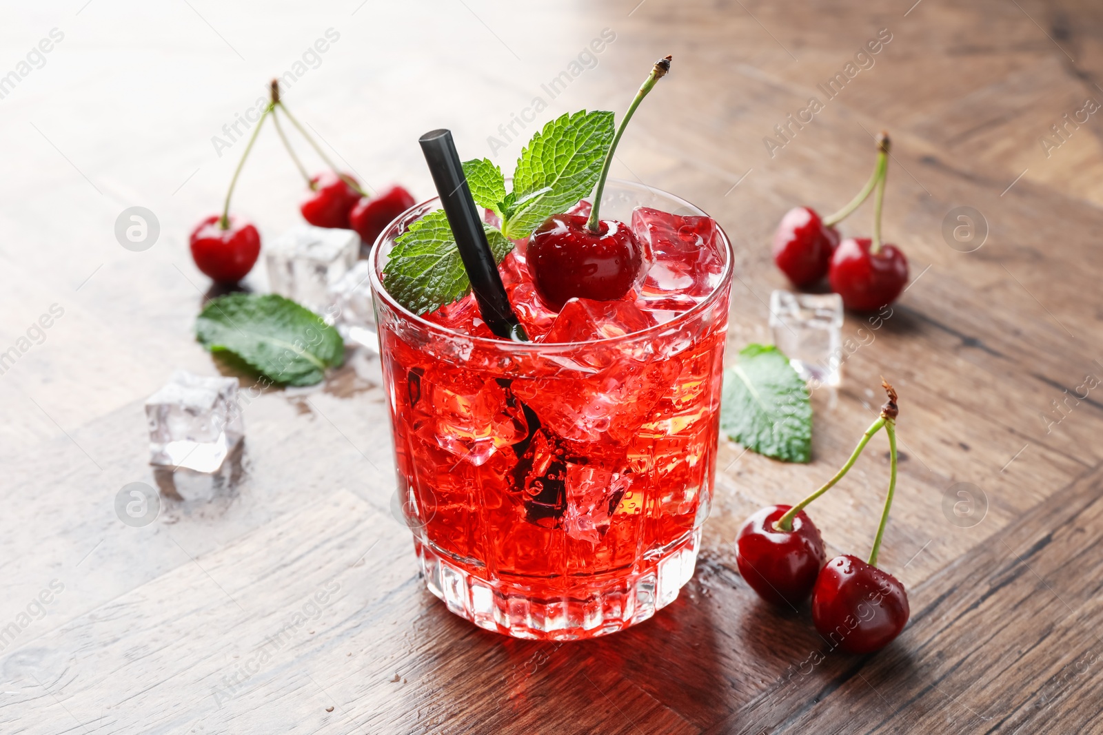 Tasty cherry soda with ice cubes, berries and mint in glass on wooden table, closeup Photo of Tasty cherry soda with ice cubes, berries and mint in glass on wooden table, closeup