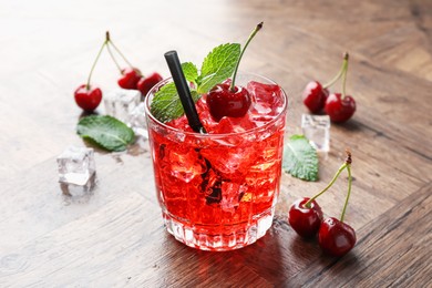 Photo of Tasty cherry soda with ice cubes, berries and mint in glass on wooden table, closeup