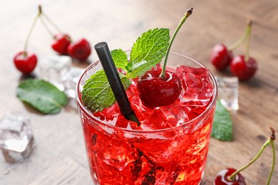 Photo of Tasty cherry soda with ice cubes, berries and mint in glass on wooden table, closeup