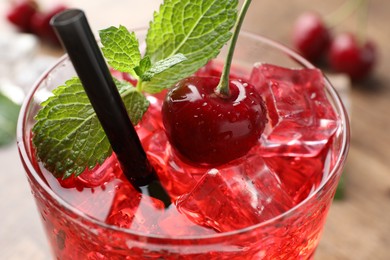 Photo of Tasty cherry soda with ice cubes, berry and mint in glass on table, closeup