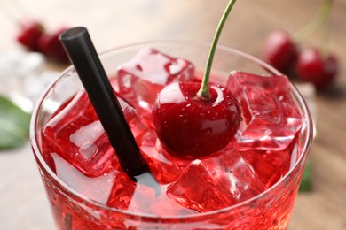 Photo of Tasty cherry soda with ice cubes and berry in glass on table, closeup