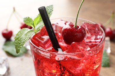 Photo of Tasty cherry soda with ice cubes, berry and mint in glass on table, closeup
