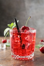 Photo of Tasty cherry soda with ice cubes, berries and mint in glass on wooden table, closeup