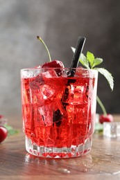 Photo of Tasty cherry soda with ice cubes, berries and mint in glass on wooden table, closeup